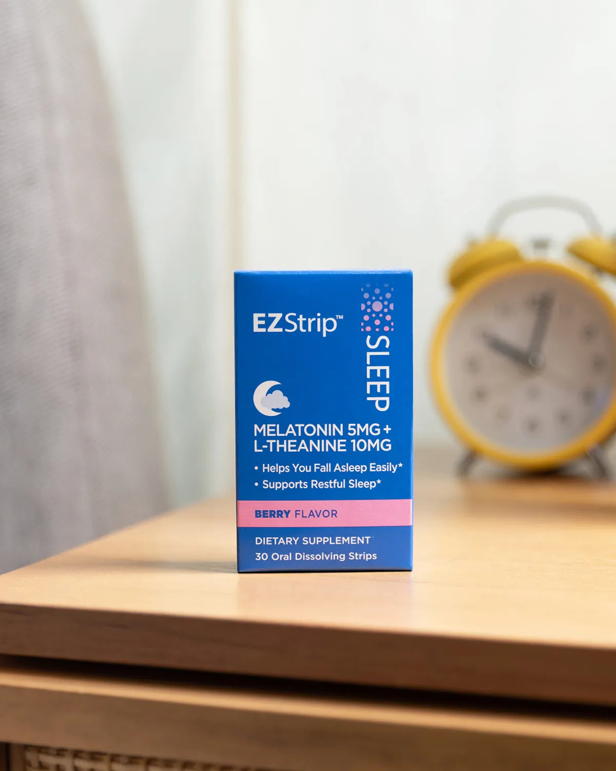 EZStrip Sleep dietary supplement box placed neatly on a wooden bedside table, with a yellow alarm clock visible in the softly blurred background.