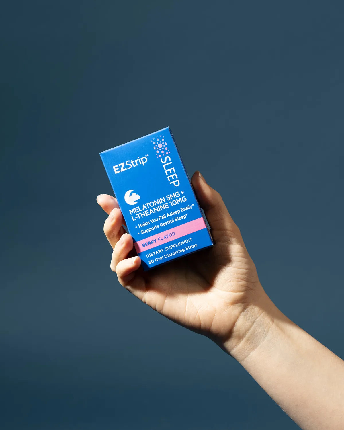 A hand holding the blue EZStrip Sleep dietary supplement box containing Melatonin and L-Theanine clearly shown against a deep blue backdrop.