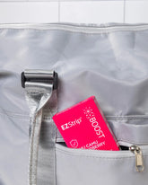 A pink EZStrip Boost box partially tucked into the front pocket of a gray travel bag.