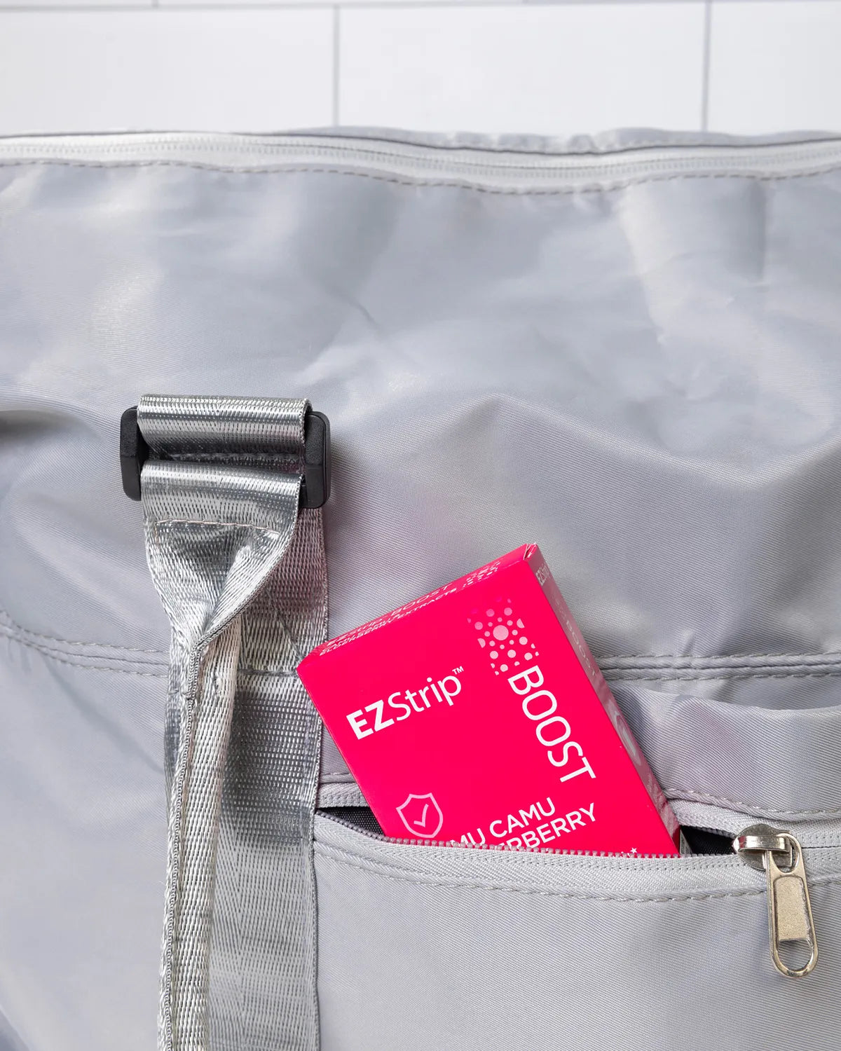 A pink EZStrip Boost box partially tucked into the front pocket of a gray travel bag.
