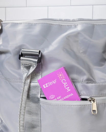 A purple EZStrip Calm box partially tucked into the front pocket of a gray travel bag.