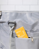 EZStrip Ginger Root Extract dietary supplement package partially placed inside the pocket of a stylish gray travel bag, positioned against white tiled background.